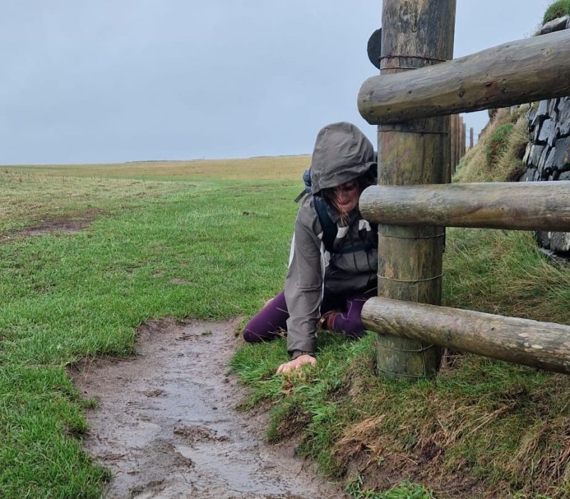 Jadine on her knees in a muddy stream on the coast path as she crawls the remaining few miles of the Cornish Coast path.